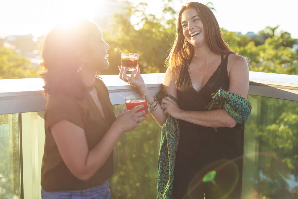 Two women laughing while drinking alcohol drinks outside