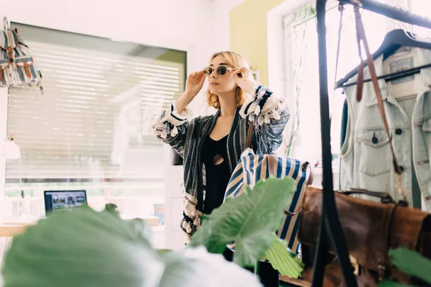 A woman trying on clothing and sunglasses in a mirror