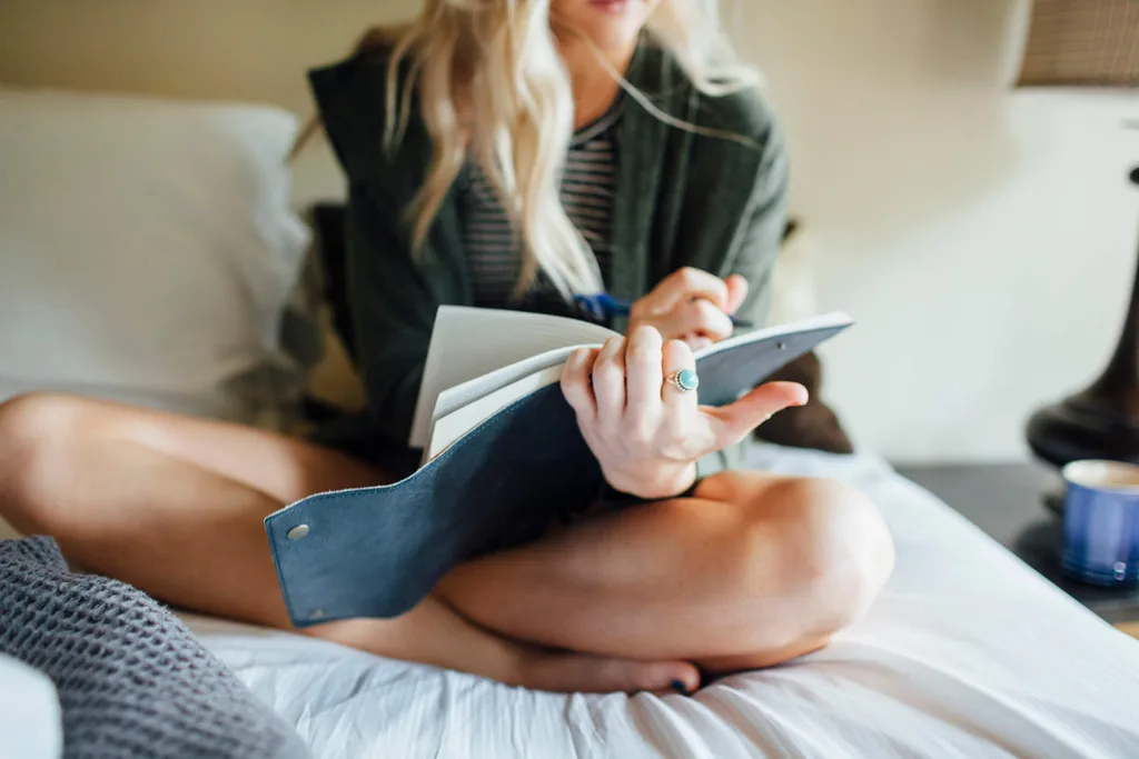 A woman writing in a journal while sitting on her bed