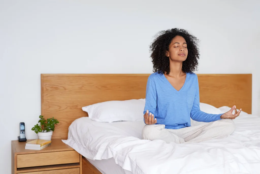 A woman meditating while sitting on a bed