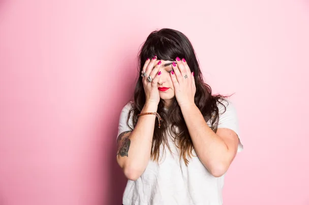 A scared woman cowering in front of a pink background
