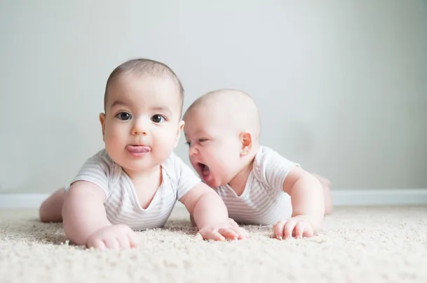 Two babies playing on a white carpet