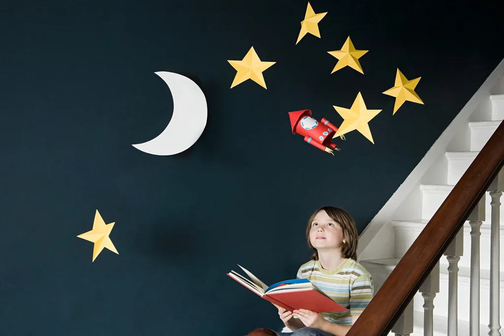A young boy reading a book under stars and a moon
