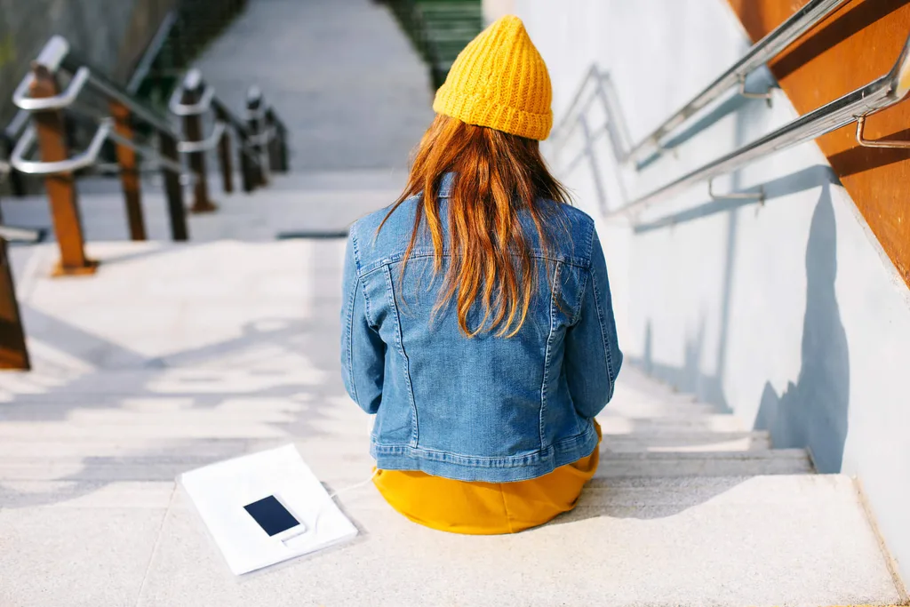 A young girl sitting on a concrete staircase with a yellow shirt, yellow beanie and denim jacket