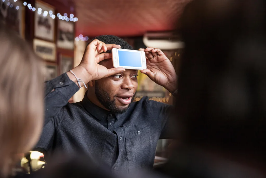 A man at a pub with his friends with a phone on his forehead