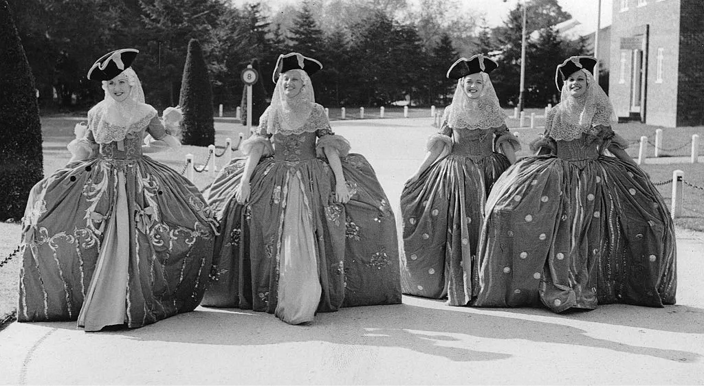 A black and white photo of women wearing hoop skirts