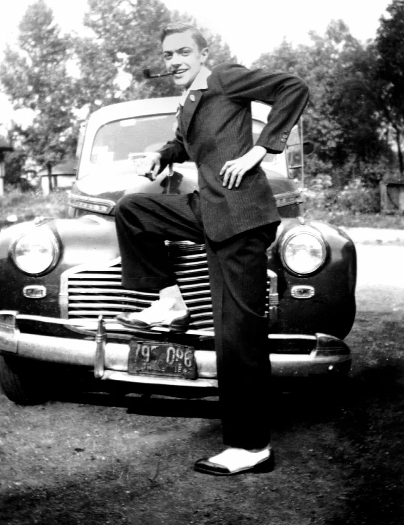 A young man in a drape suit standing on a car