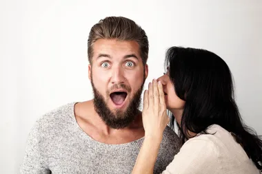 A woman whispering into a man's ear who looks surprised