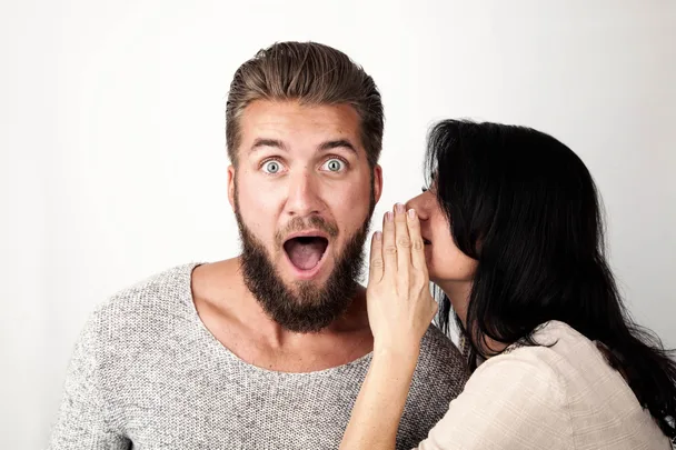 A woman whispering into a man's ear who looks surprised