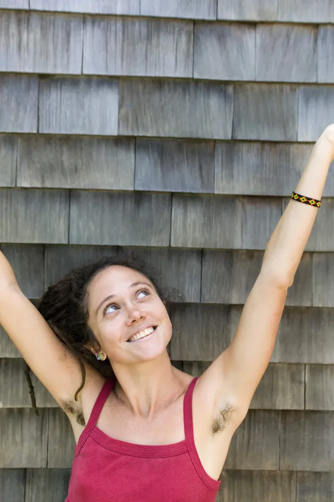 A young woman with hairy armpits raising her arms
