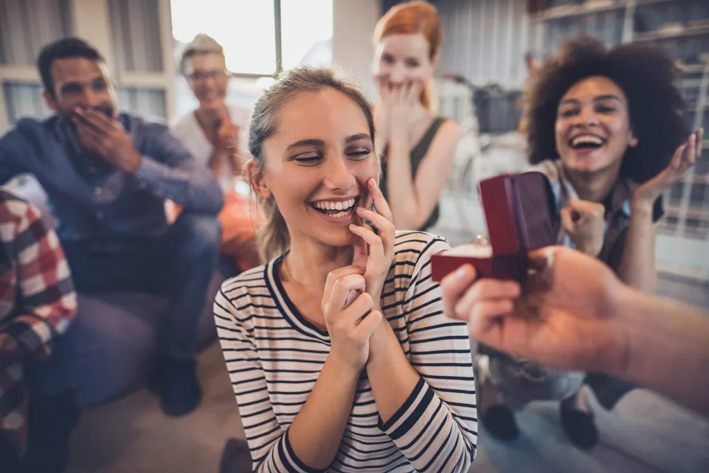 A woman smiling as she's being proposed to in front of friends