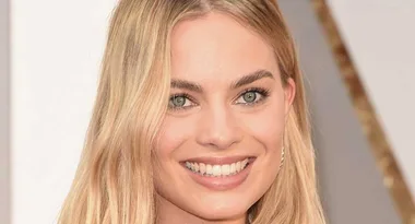 Margot Robbie smiling with long blonde hair and green eyes, honored in Time 100 Most Influential People list.