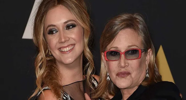 Two women posing on the red carpet, one younger with blonde hair and the other with glasses.