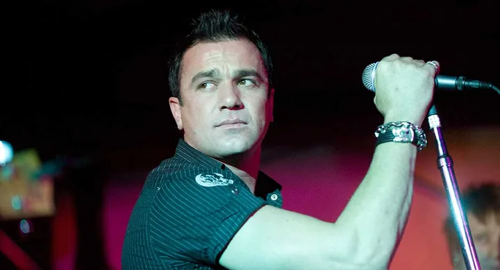 A man with short dark hair holding a microphone and looking to the side.