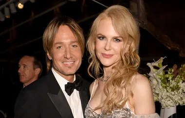 Two people dressed elegantly, likely at a formal event, with flowers in the background.