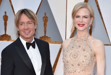 Couple posing on the Oscars red carpet, with elegant attire and award statues in the background.