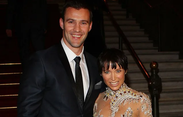 A couple in formal attire smiles at an event, standing on a staircase.