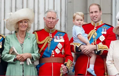 A group of people standing on a balcony, two wearing red military uniforms, one holding a child.