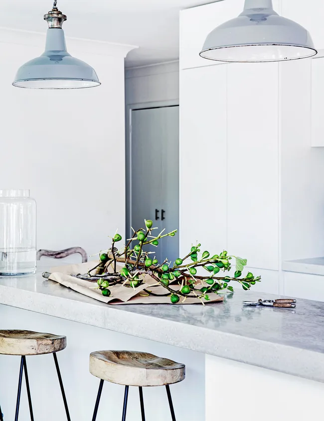 Industrial lighting softens a minimal white kitchen.