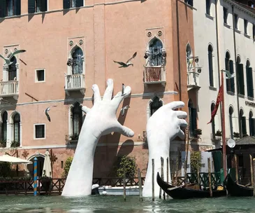 A sculpture of colossal hands rise from Venice canal