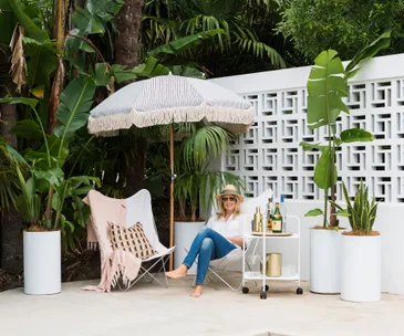 shelley ferguson sitting on outside chair under an retro style fringed umbrella