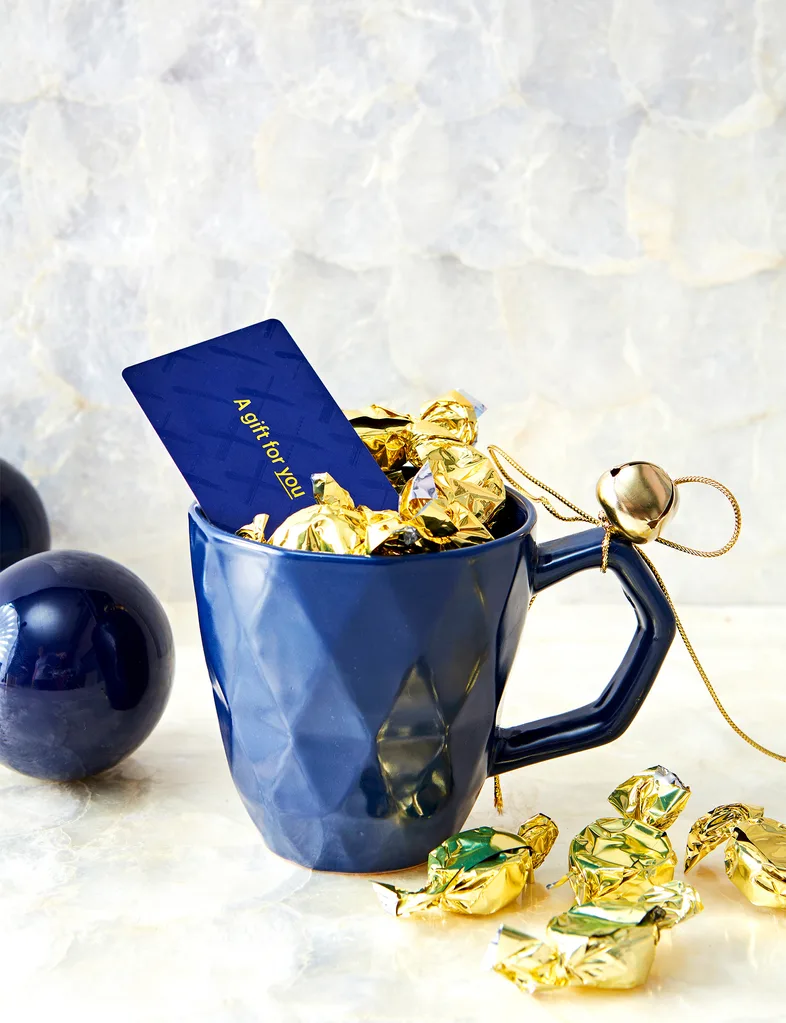 A gift voucher inside a blue mug with some golden sweets.
