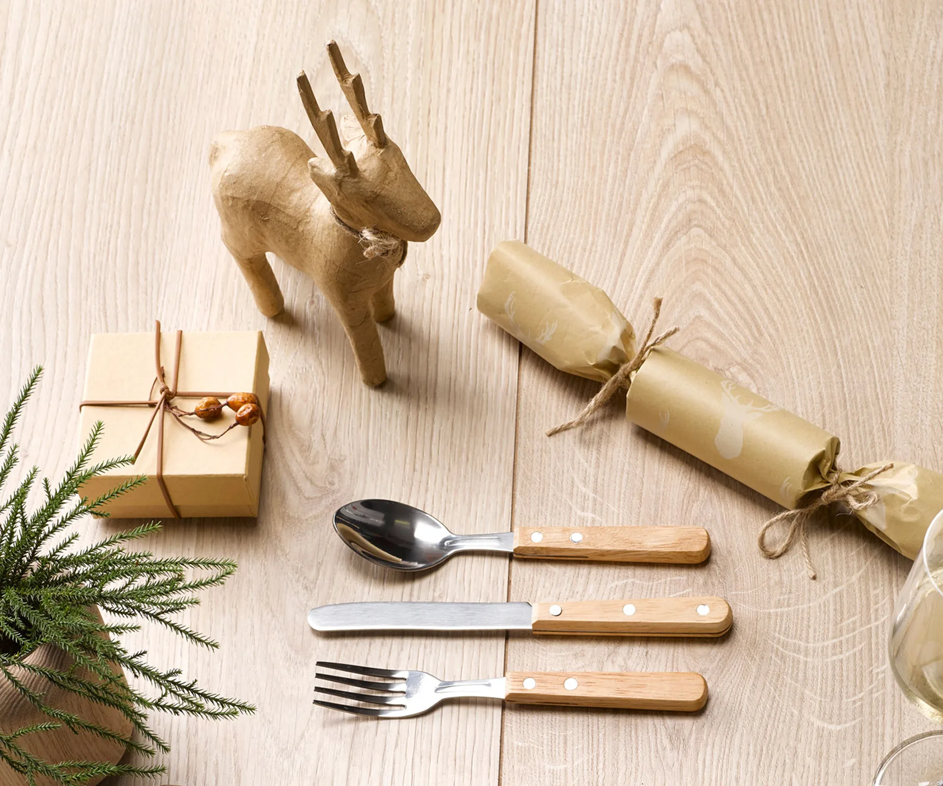 A rustic-style Christmas cracker made from craft paper, as well as a cutlery set and a wooden toy animal. 