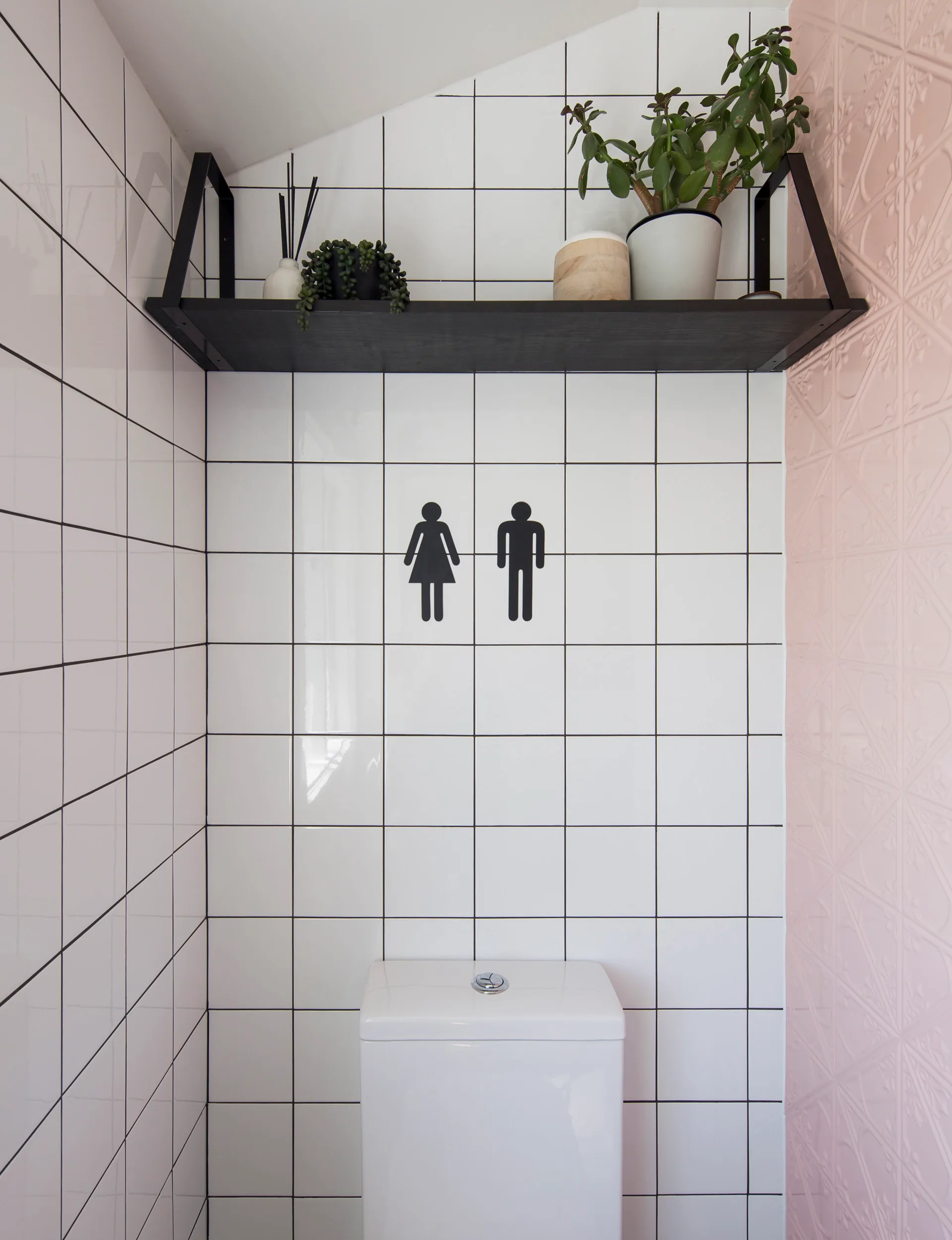 Pink walls with white tiles around the toilet in the black white and pink bathroom