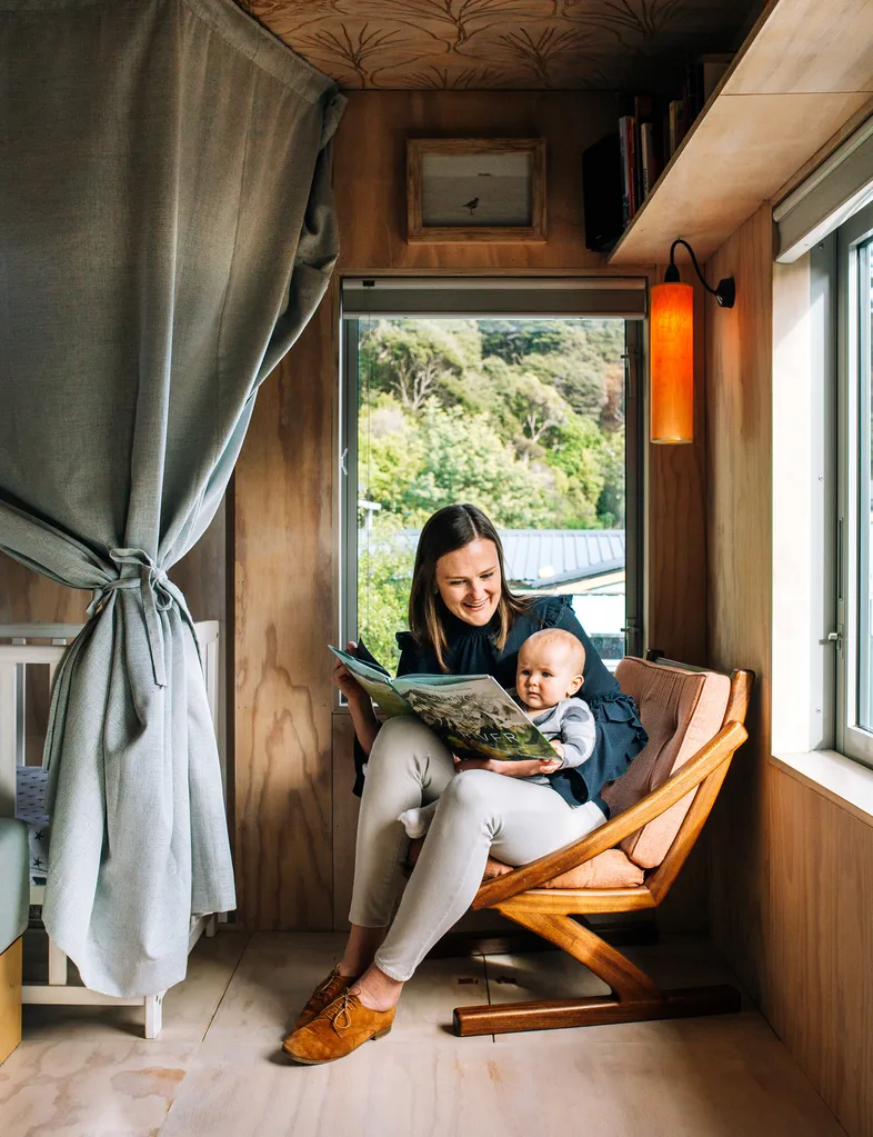 The shipping container home owner reading to her baby in the armchair in the corner