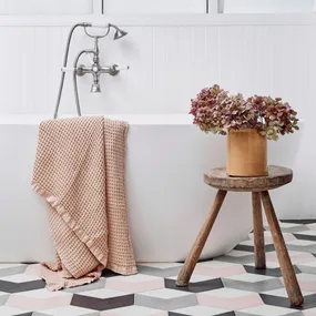 A bath with a pink towel draped over the side, a wooden stool holding a pot plant to the side and pink, white and grey chequered flooring beneath to showcase the flooring trends