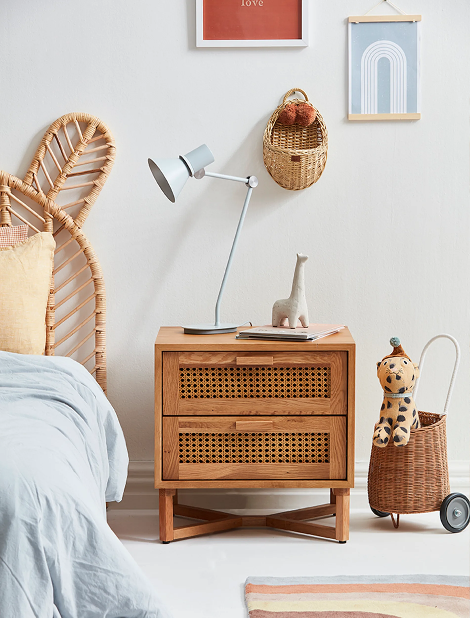 A gender neutral coloured bedside table with a light blue duvet cover over the bed