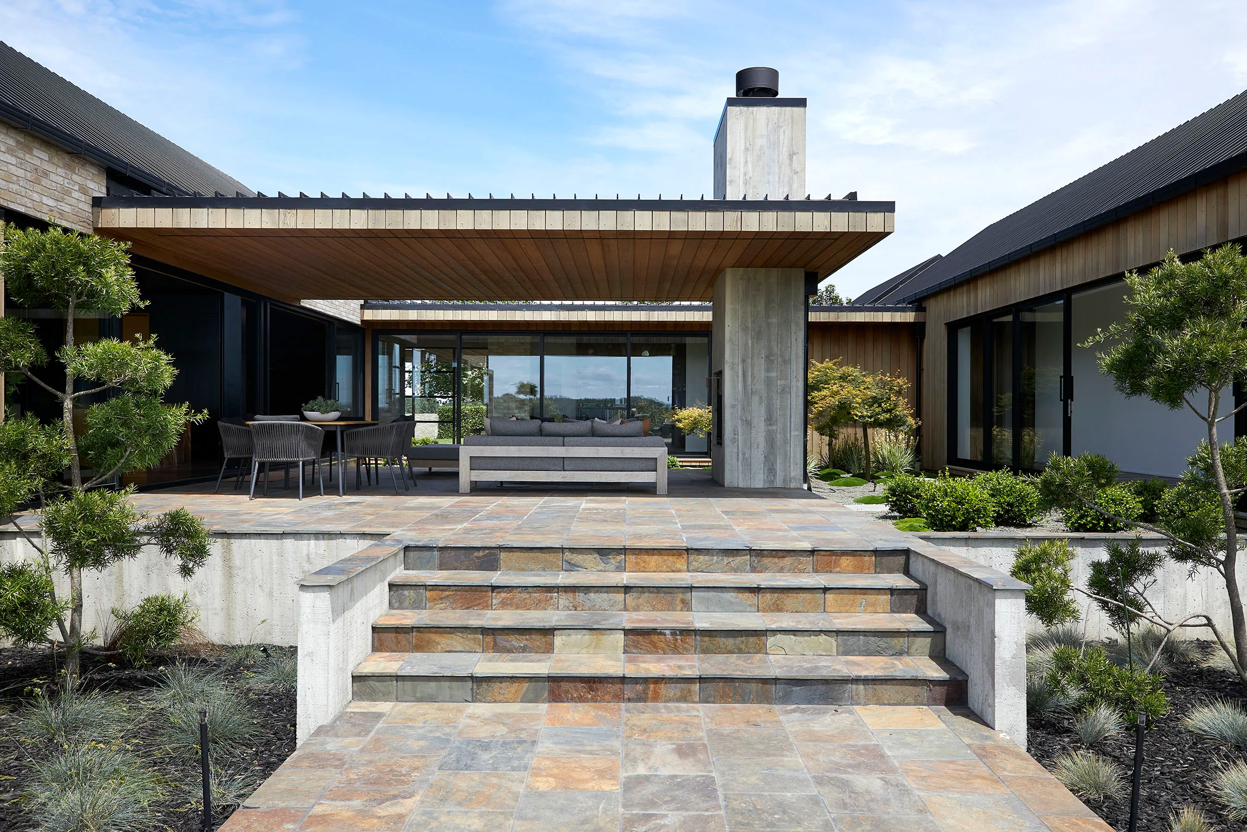 Modern house exterior with large patio, outdoor seating, and landscaped garden.