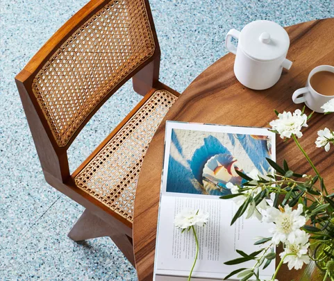 Wooden chair and table setting with a book, white flowers, a teapot, and a cup of tea.