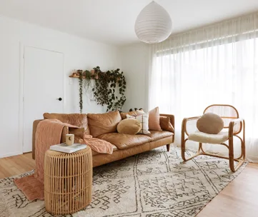 Cozy living room with a brown leather sofa, rattan chair, plants, and soft lighting.