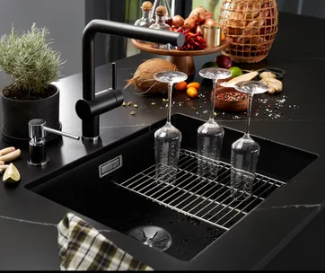 Wine glasses drying upside down on a black kitchen sink with spices and ingredients on the counter nearby.