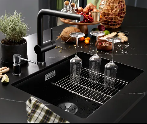 Wine glasses drying upside down on a black kitchen sink with spices and ingredients on the counter nearby.