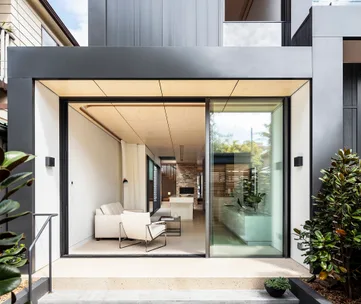 Modern living room with large glass doors, white sofa, and minimalist decor, opening to an outdoor area.