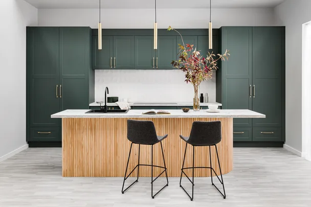 Modern kitchen with green cabinets, marble countertop, wooden island, open book, vase, and two bar stools.