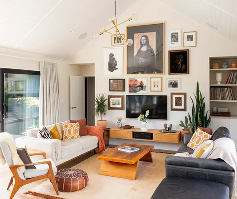 Living room with a gallery wall, modern furniture, plants, and a wooden coffee table, featuring framed pictures.