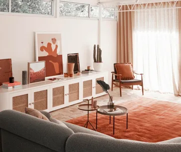 Warm, modern living room with art, gray sofa, orange rug, and armchair near window with curtains.