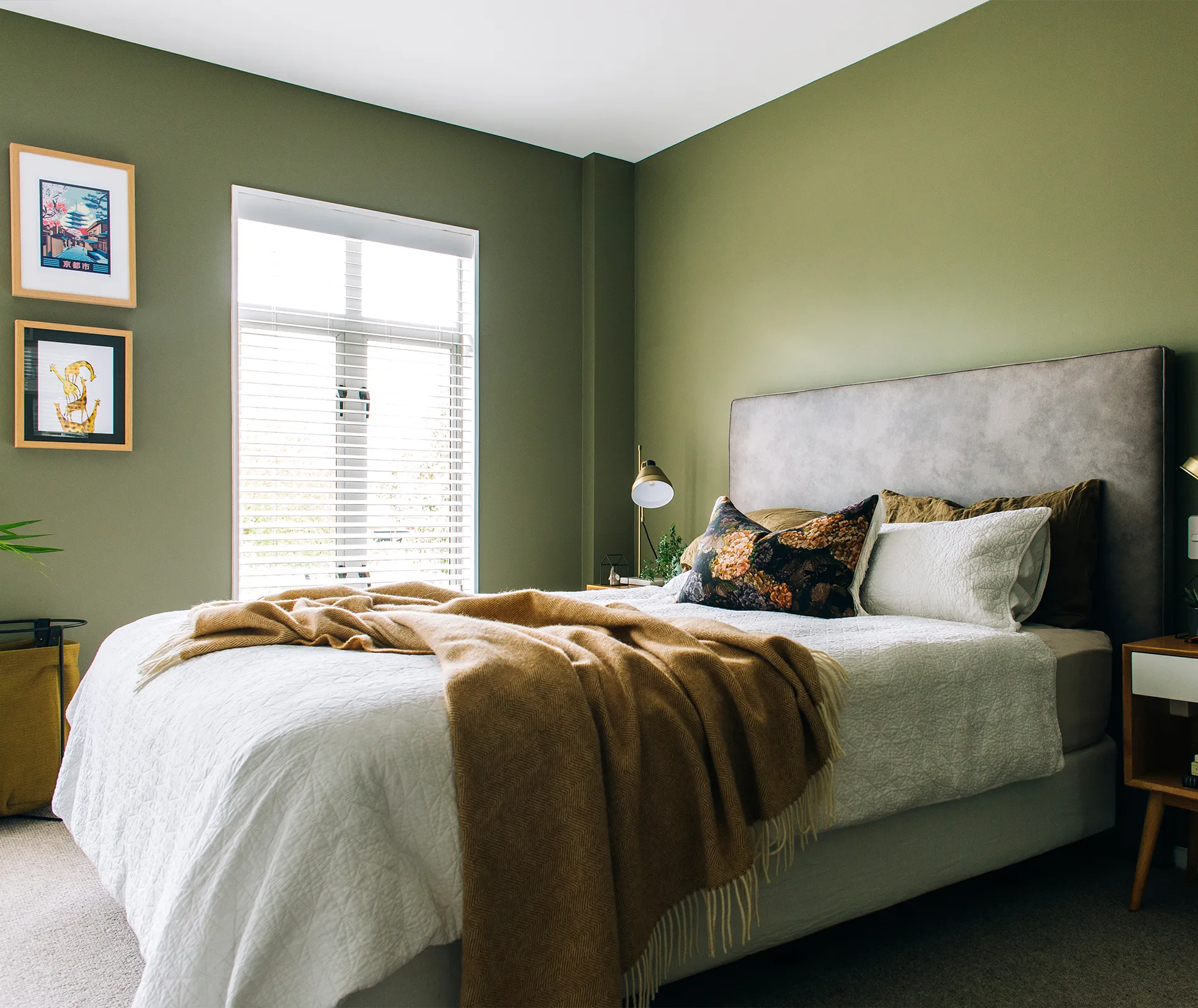 Green-walled bedroom with a large bed, gray headboard, white bedding, tan throw blanket, and two framed pictures on the wall.