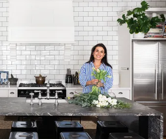 A woman in a striped shirt holding flowers in a modern kitchen with a marble island and stainless steel appliances.