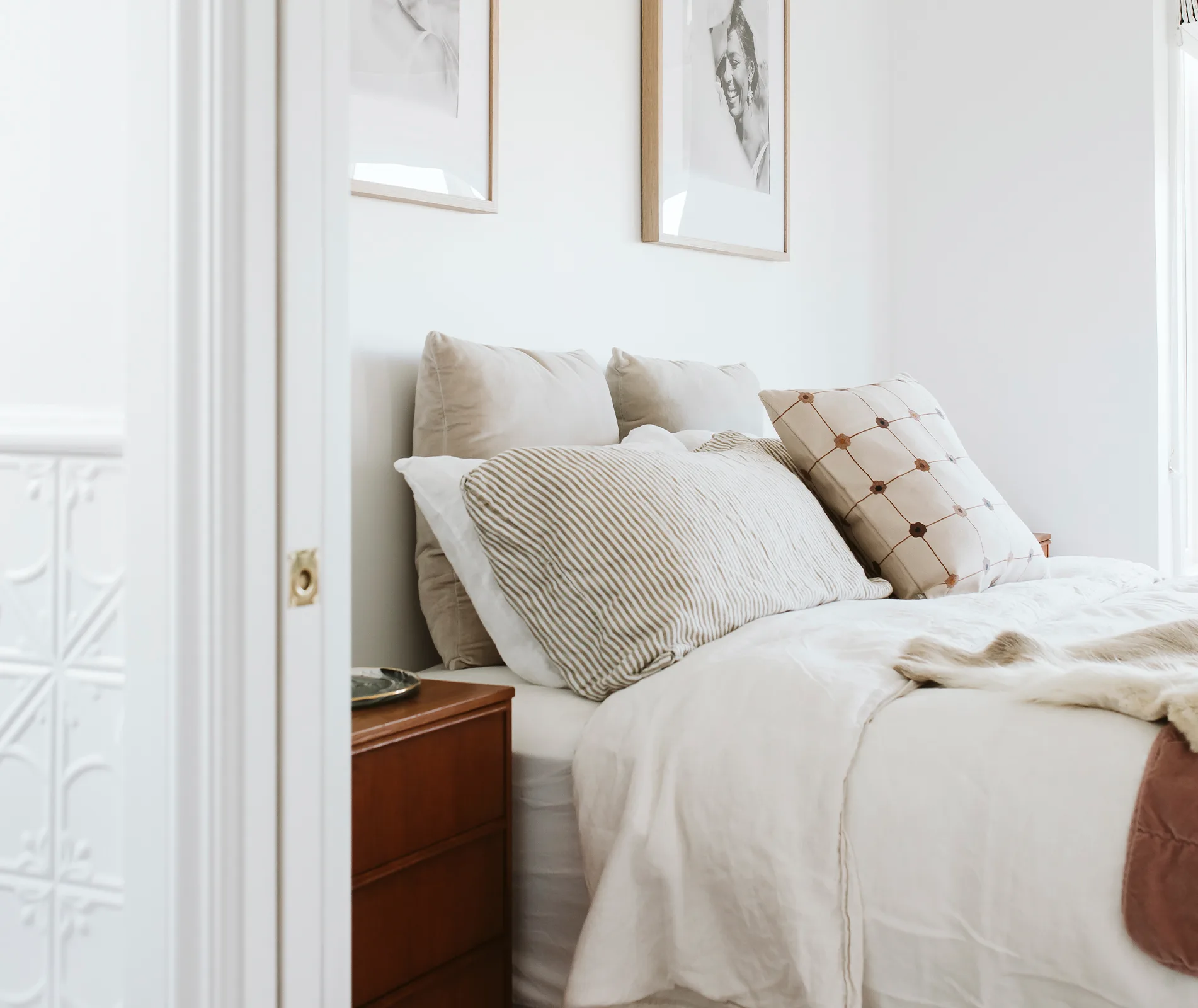 Cozy bedroom with a neatly made bed, various pillows, and framed black and white photos on the wall.
