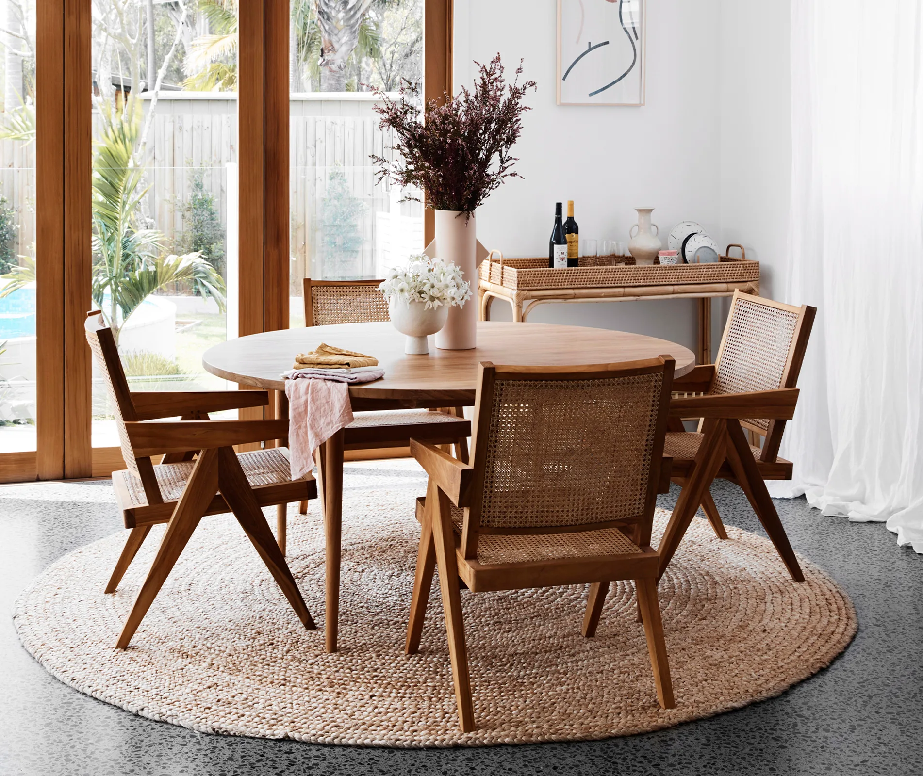 Stylish dining area with a round wooden table, four chairs, and decorative plants near large windows.