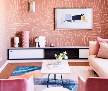 Stylish living room with abstract art, decorative vases, and cozy pink seating against patterned wallpaper.