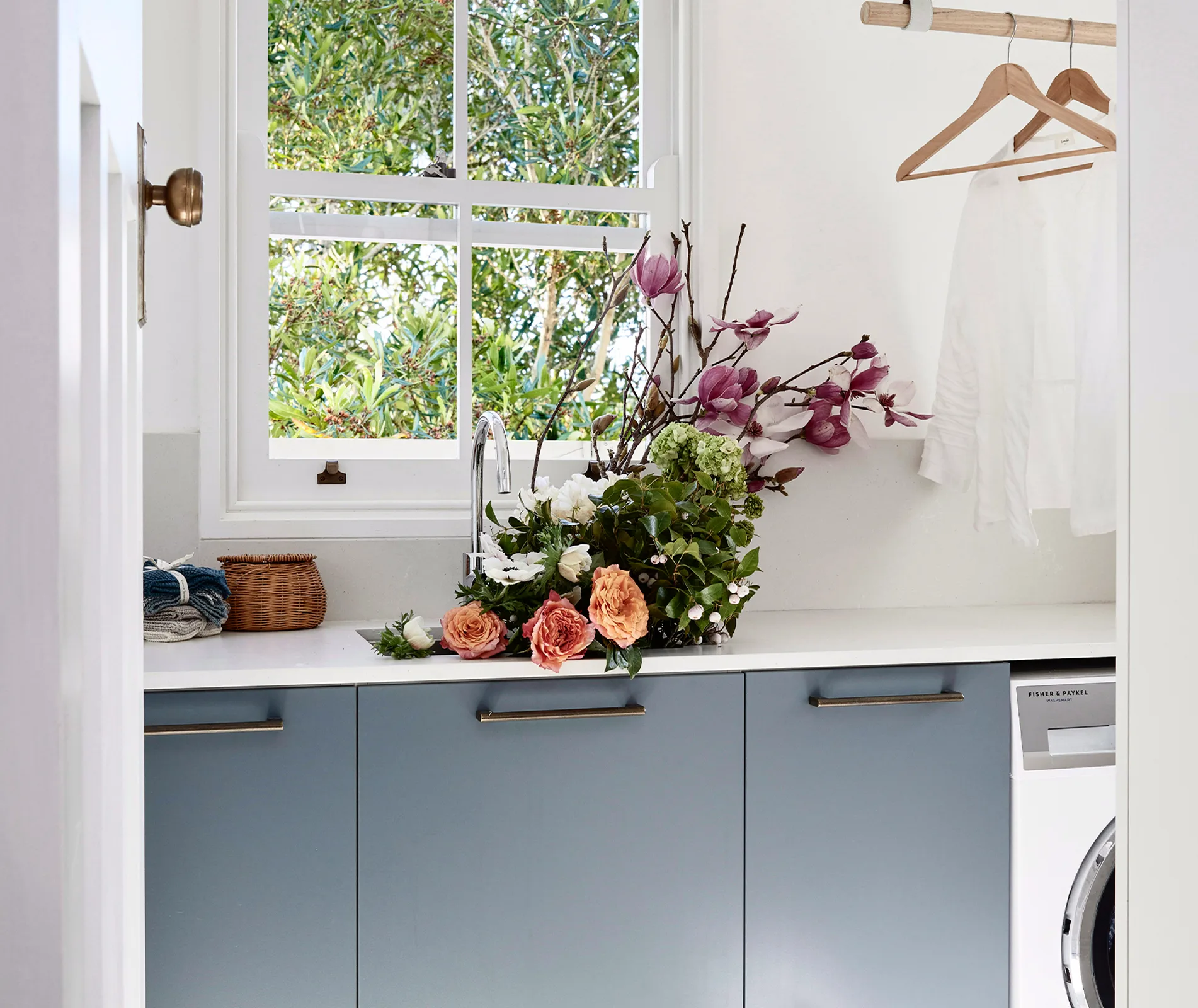 Laundry room with a window, flowers on the counter, a wicker basket, and a clothes rack with hangers.
