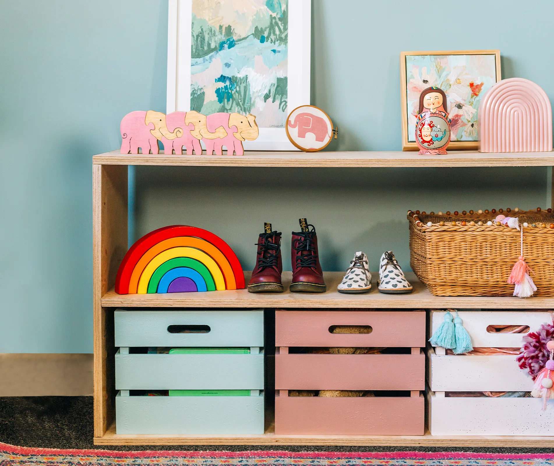 Shelf with toys, shoes, and baskets: wooden elephants, rainbow stacker, toddler boots, and colorful storage boxes.