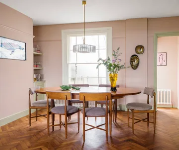 Mid-century modern dining room with round wooden table, six chairs, brass chandelier, and floral centerpiece.