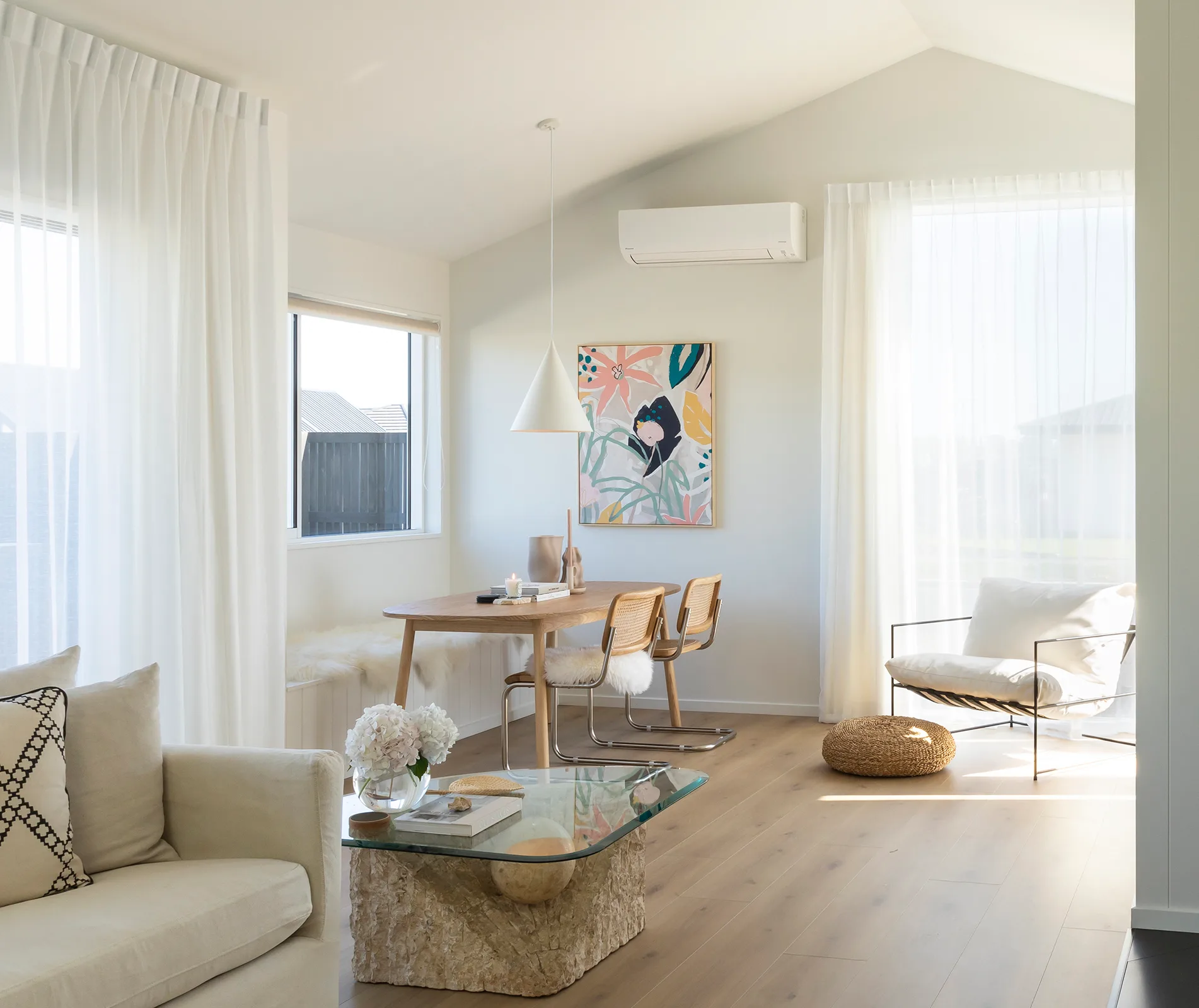 Bright, modern living room with neutral decor, featuring a wooden dining table, chairs, and abstract wall art.