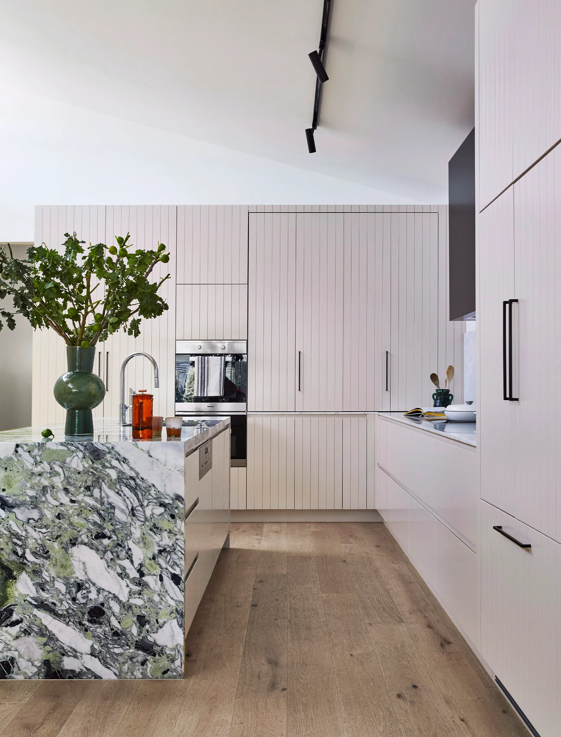 Modern kitchen with white cabinets, green marble island, wooden floor, and plants in a vase.